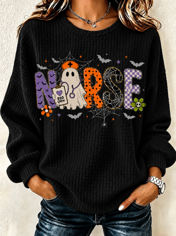 A woman wearing a black ribbed knit sweater with a colorful Halloween-themed 'Nurse' graphic, paired with blue jeans.