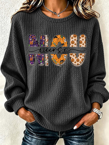 A woman wearing a dark gray waffle-knit crewneck sweatshirt with a 'MOON NURSE' graphic across the chest. The letters of 'MOON' feature Halloween-themed patterns including pumpkins, ghosts, and spiderwebs, while 'NURSE' is written in black script.