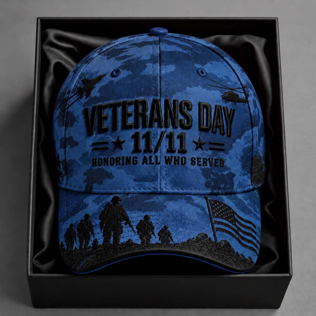 A blue camouflage baseball cap with black printed graphics and text reading 'VETERANS DAY 11/11 HONORING ALL WHO SERVED,' displayed inside a black gift box with satin lining.