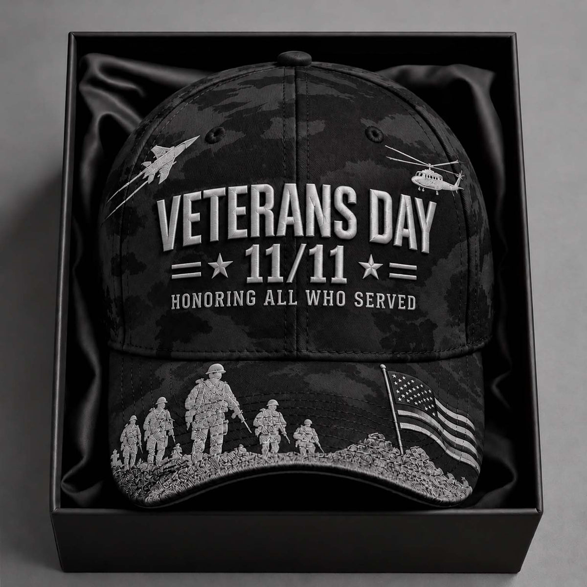 A black camouflage baseball cap with white 'Veterans Day 11/11 Honoring All Who Served' text and military-themed graphics, displayed inside a black gift box on a dark gray background.