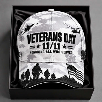 A Veterans Day baseball cap with a black and white camouflage pattern, featuring silhouettes of soldiers, military aircraft, and an American flag, displayed inside a black gift box.