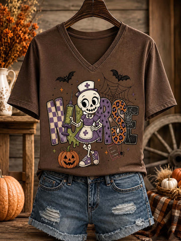 A brown V-neck graphic T-shirt hanging on a wooden hanger, styled with distressed denim shorts in a rustic autumn-themed setting with pumpkins and fall decor.