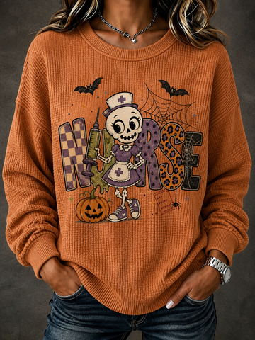 A woman wearing a burnt orange waffle-knit crewneck sweater with a large Halloween nurse graphic on the front, paired with blue jeans against a dark gray background.