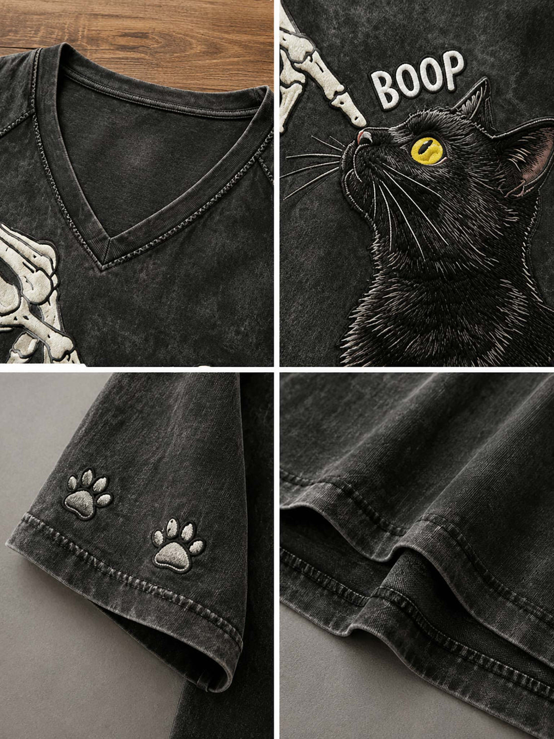 A dark gray washed V-neck t-shirt with a graphic of a skeleton hand biting a black cat's nose, with the word 'BOOP' and paw prints on the sleeves, shown hanging on a wooden hanger with blue denim shorts against a gray background.