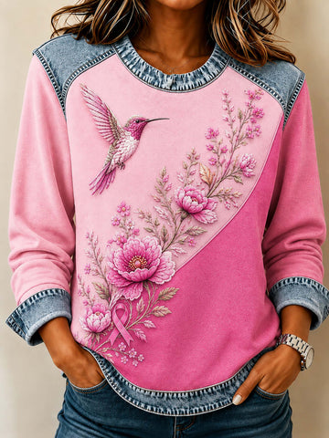 A woman wearing a pink long-sleeve top with a diagonal split design, featuring a large pink flower and hummingbird graphic on one side and a cuffed denim-style sleeve and hem.