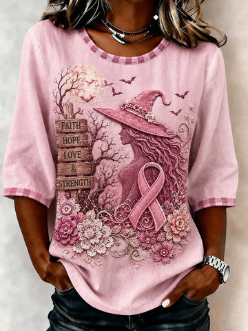A woman wearing a pink 3/4 sleeve graphic t-shirt with a witch, pink ribbon, flowers, and the words 'FAITH HOPE LOVE & STRENGTH' printed on the front.