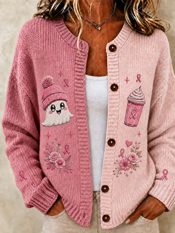 A woman wearing a pink chunky knit cardigan with embroidered designs, including a ghost, a pink drink cup, roses, and pink awareness ribbons, over a white tank top.