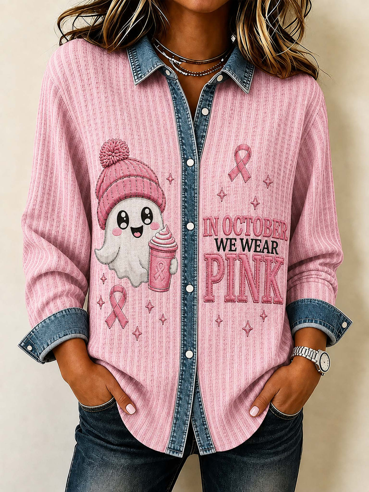 A woman wearing a pink long-sleeve button-up shirt with a denim collar and cuffs, featuring a cute ghost graphic and the text 'IN OCTOBER WE WEAR PINK' on the front.