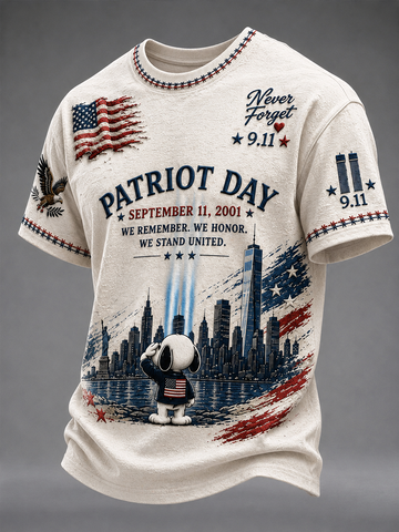 A cream-colored short-sleeve t-shirt featuring a detailed patriotic 9/11 themed graphic print with Snoopy, the New York City skyline, and American flag motifs, set against a neutral gray background.
