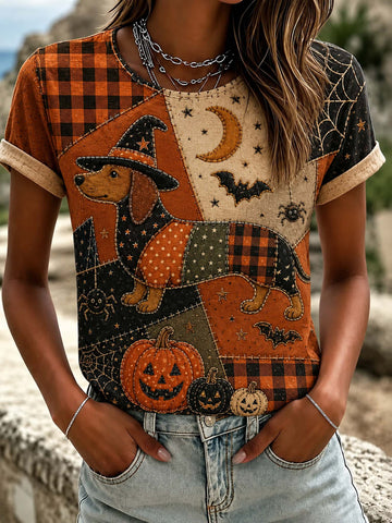 A woman wearing a short-sleeve Halloween-themed patchwork t-shirt with a dachshund, pumpkins, bats, and spider motifs, paired with light-wash denim jeans.