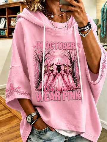A person wearing a pink oversized hoodie with a graphic print that reads 'IN OCTOBER WE AR PINK' and shows a mirror selfie in an indoor setting.