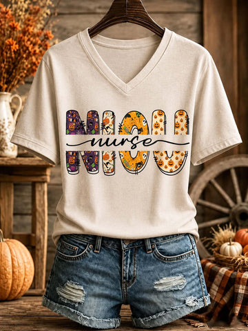 A beige V-neck t-shirt with a 'MOM NURSE' graphic featuring Halloween-themed letter designs, styled on a hanger with denim shorts against a rustic fall-themed background.