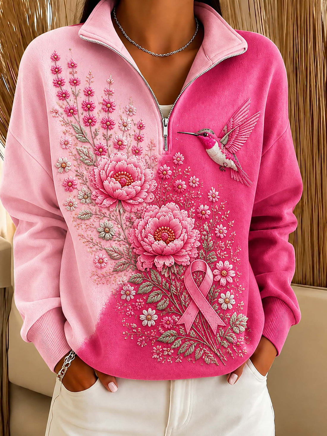 A pink quarter-zip sweatshirt with a floral and hummingbird graphic, worn by a model in front of a bamboo screen.
