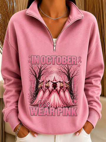 A woman wearing a pink quarter-zip sweatshirt with a 'We Wear Pink' breast cancer awareness graphic on the front, featuring a witch's hat and figures in pink dresses.