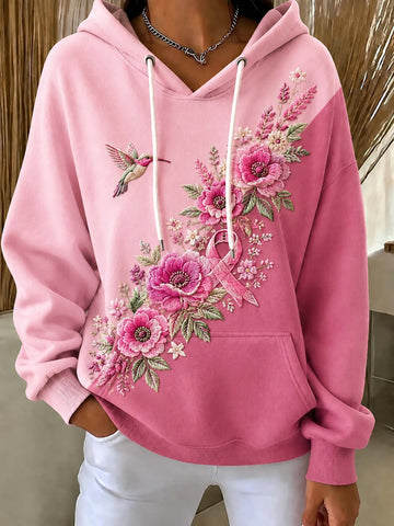 A pink pullover hoodie with white drawstrings, featuring a large floral and butterfly embroidery design on the front. The model is wearing white pants and a silver necklace, standing in an indoor setting.