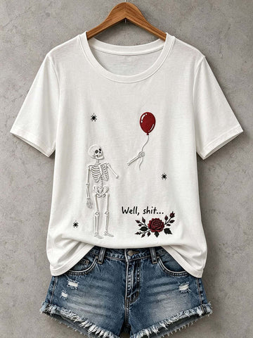 A white short-sleeve graphic T-shirt hanging on a wooden hanger against a gray textured wall, styled with distressed denim shorts. The shirt features a black line-art skeleton, a red balloon, the text 'Well, shit.