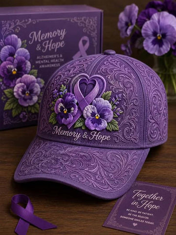 A purple embroidered baseball cap with floral and ribbon embroidery, shown with a matching purple gift box and a purple awareness ribbon on a wooden surface. The cap reads 'Memory & Hope' and the box also reads 'Memory & Hope' for Alzheimer's & Mental Health Awareness.