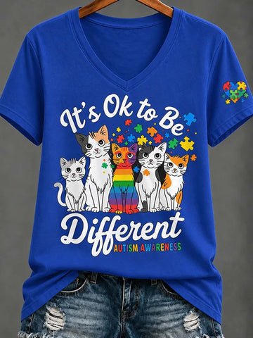 A royal blue V-neck t-shirt featuring an autism awareness graphic with six cats in front of a rainbow and puzzle-piece design, paired with distressed denim jeans on a hanger against a gray background.