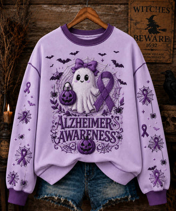 A lavender-purple crewneck sweatshirt with a Halloween-themed Alzheimer's Awareness graphic, hanging on a wooden hanger against a rustic, themed background with denim jeans partially visible underneath.