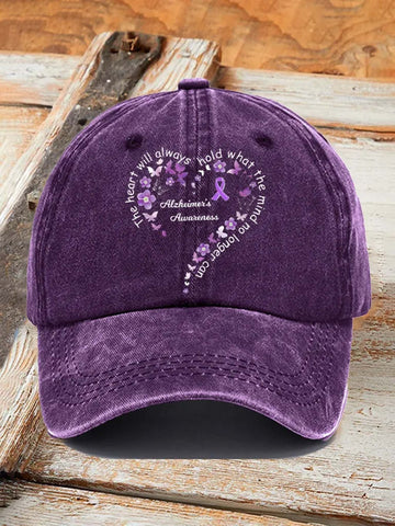 A purple washed baseball cap with a Alzheimer's Awareness graphic on the front, displayed on a rustic wooden surface.