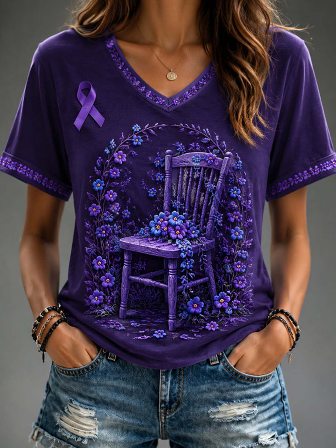 A woman wearing a purple V-neck graphic T-shirt with a purple awareness ribbon and a floral chair design, paired with distressed denim shorts.