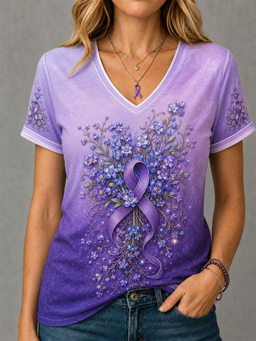 A woman wearing a purple V-neck t-shirt with a floral bouquet and purple awareness ribbon graphic on the front, paired with blue jeans against a gray background.