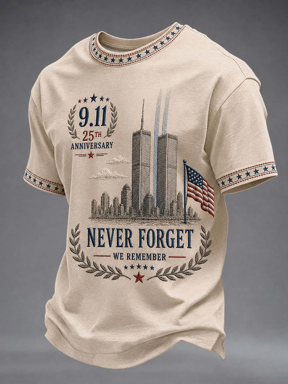A beige short-sleeve t-shirt with a 9/11 memorial graphic, featuring the Twin Towers, an American flag, and the text '9.11 25th Anniversary Never Forget We Remember'.