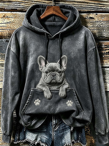 A dark gray mineral-wash hoodie with a detailed graphic of a French Bulldog peeking out of the front kangaroo pocket, styled with denim shorts on a rustic wooden plank background.