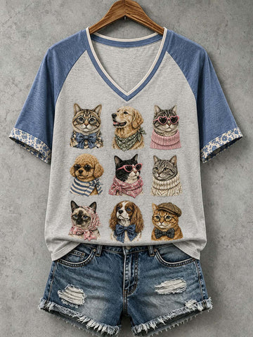A women's raglan V-neck T-shirt with a light heather gray body and blue sleeves, featuring a graphic print of nine cute illustrated pet portraits (cats, dogs, and a French bulldog). The shirt is styled with distressed denim shorts on a wooden hanger against a textured gray background.