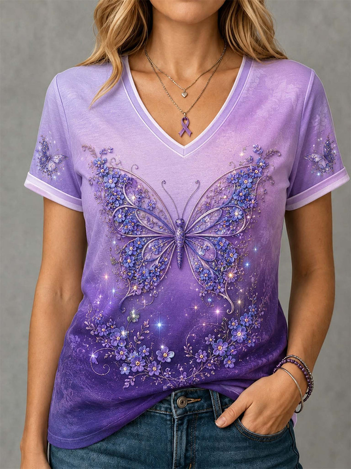 A woman wearing a purple V-neck short-sleeve t-shirt with a large glittery butterfly and floral graphic on the front, paired with blue jeans.