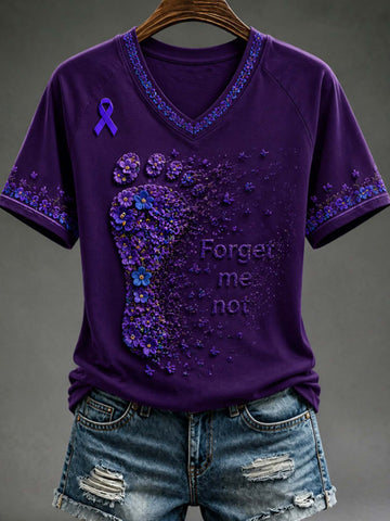 A purple short-sleeve V-neck T-shirt with a large purple foot-shaped floral design, a purple awareness ribbon on the left chest, and the words 'Forget me not' printed on the front, shown hanging on a wooden hanger with distressed denim shorts against a dark gray background.