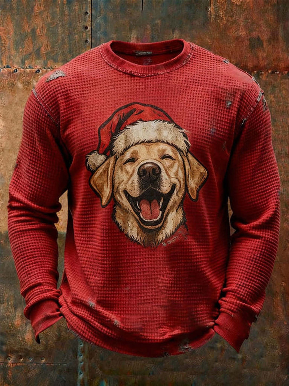 A red waffle-knit crewneck sweatshirt featuring a graphic of a golden retriever dog wearing a Santa hat, displayed against a rustic, textured brown metal background.