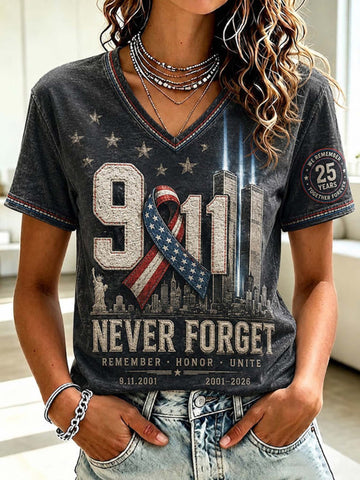 A woman wearing a dark gray V-neck graphic t-shirt with a '9/11 Never Forget' design featuring the New York City skyline, a patriotic ribbon, and 'Remember Honor Unite' text, paired with light wash denim jeans.