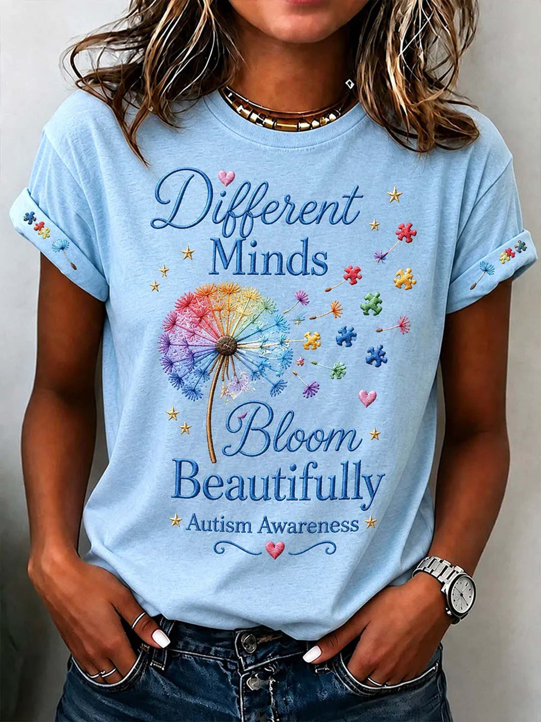 A woman wearing a light blue graphic t-shirt with a dandelion design and the text 'Different Minds Bloom Beautifully Autism Awareness'.