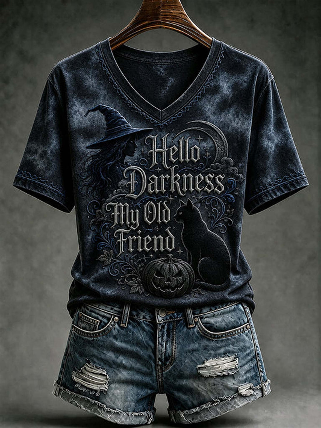 A dark acid-wash V-neck t-shirt with a Halloween graphic reading 'Hello Darkness My Old Friend' featuring a witch hat, cat, and pumpkin, styled on a wooden hanger with distressed denim shorts against a dark gray background.