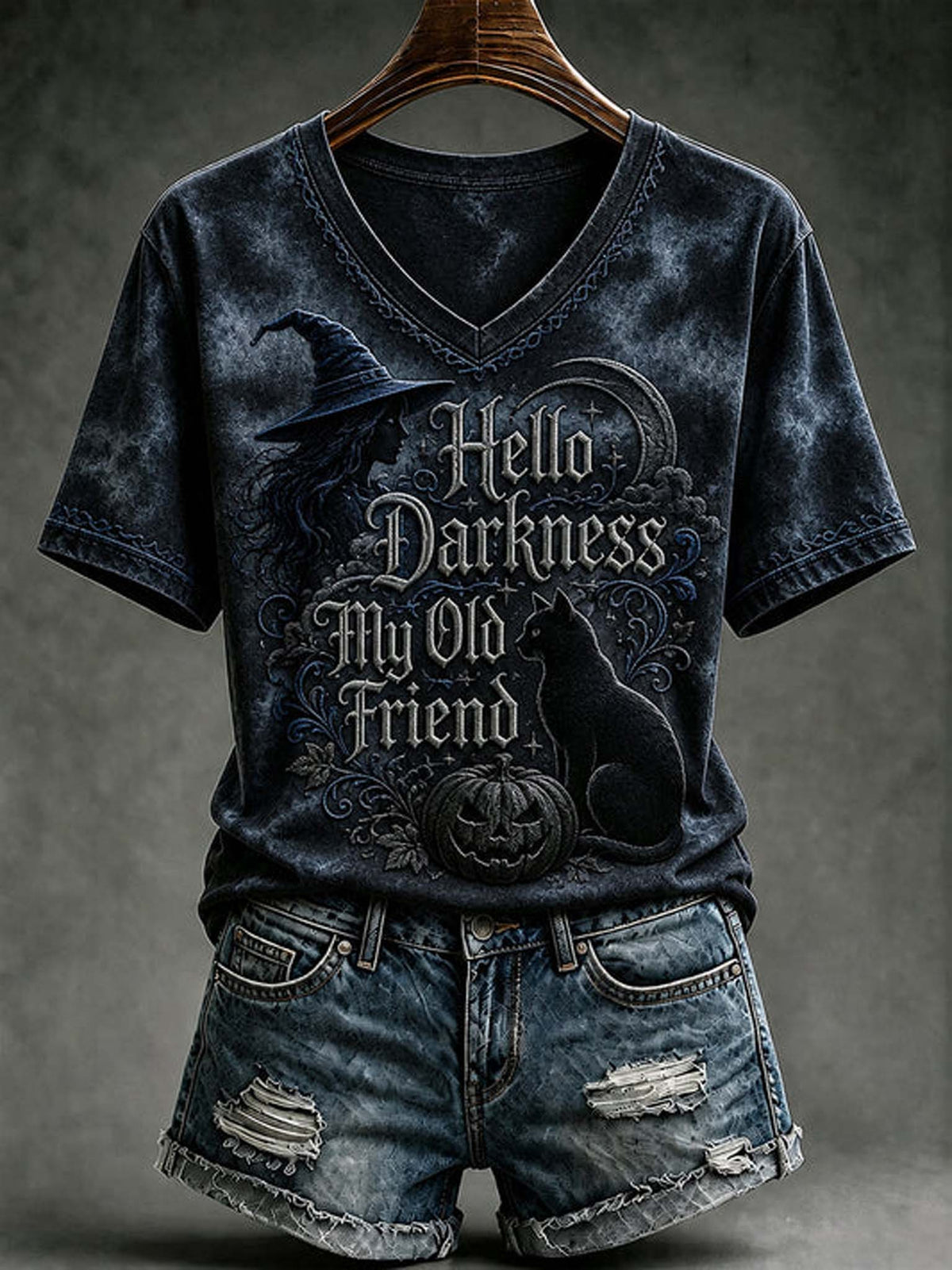 A dark acid-wash V-neck t-shirt with a Halloween graphic reading 'Hello Darkness My Old Friend' featuring a witch hat, cat, and pumpkin, styled on a wooden hanger with distressed denim shorts against a dark gray background.