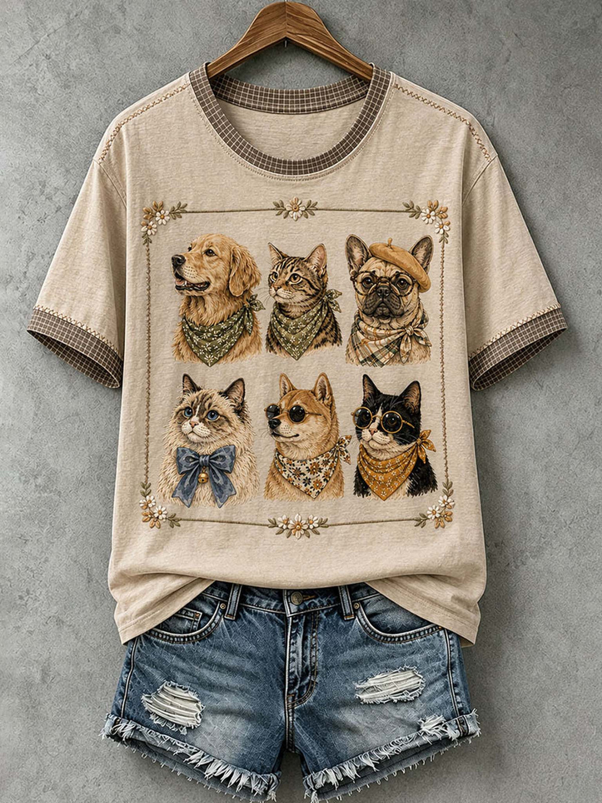 A beige graphic t-shirt with a dog print, styled with distressed denim shorts on a wooden hanger against a gray textured wall.