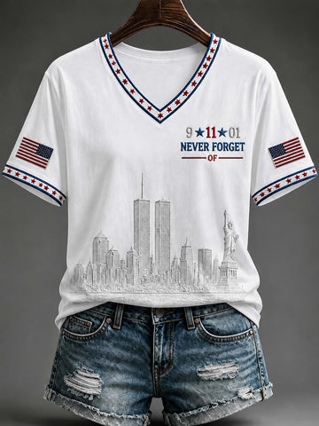 White V-neck t-shirt with a patriotic design featuring the New York City skyline, '9-11-01 NEVER FORGET' text, and American flag prints on the sleeves, styled on a hanger with distressed denim shorts against a dark gray background.