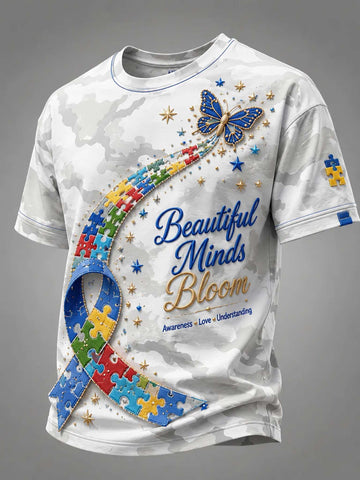 A white short-sleeve t-shirt with a subtle gray camouflage pattern, featuring a colorful graphic design for autism awareness. The design includes a blue ribbon made of puzzle pieces, a blue butterfly, gold stars, and the text 'Beautiful Minds Bloom' in blue and gold script.