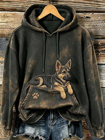 A dark brown acid-wash hoodie with a German Shepherd graphic printed on the front, styled on a wooden hanger over blue denim jeans against a rustic wooden plank background.