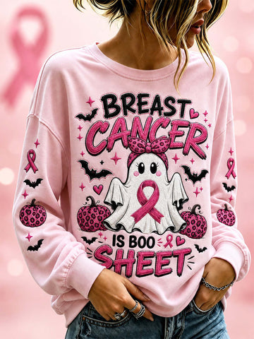 A woman wearing a light pink long-sleeve sweatshirt with a 'Breast Cancer is Boo Sheet' Halloween graphic featuring a ghost, pumpkins, bats, and pink ribbons.