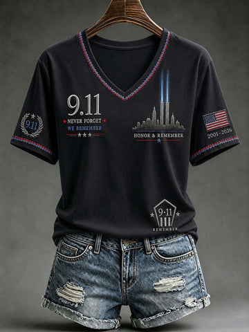 A black V-neck t-shirt with 9/11 themed graphics, shown on a wooden hanger with distressed denim shorts against a dark gray studio background.