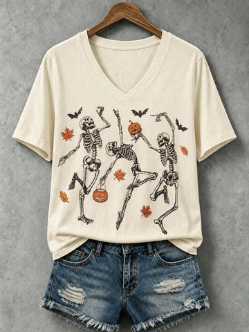 An off-white V-neck t-shirt with a graphic of three dancing skeletons, pumpkins, bats, and autumn leaves, styled on a wooden hanger with distressed denim shorts against a textured gray background.